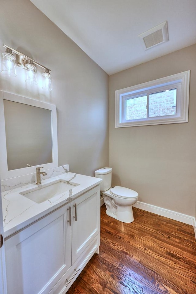 half bathroom featuring toilet, wood finished floors, visible vents, vanity, and baseboards