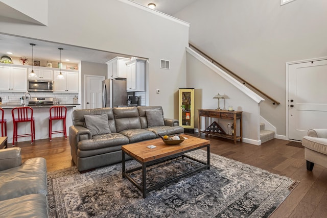 living area with visible vents, dark wood finished floors, baseboards, stairway, and high vaulted ceiling