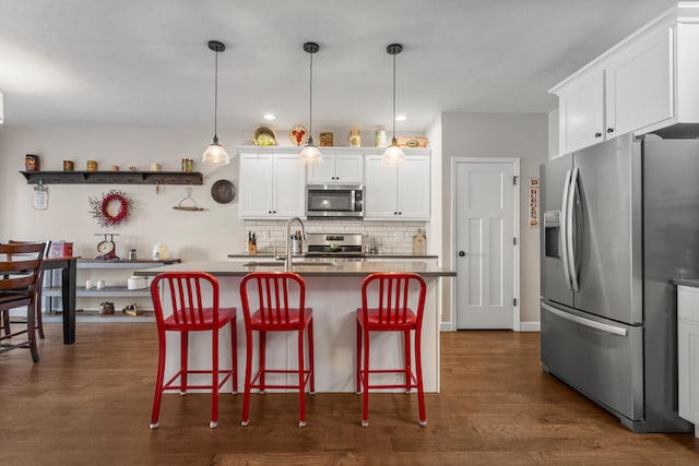 kitchen with a breakfast bar, pendant lighting, stainless steel appliances, white cabinets, and an island with sink