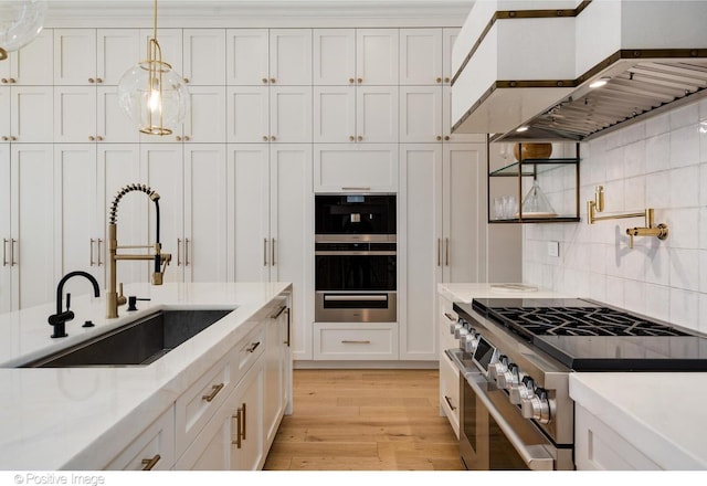 kitchen featuring wall chimney range hood, range with two ovens, a sink, and white cabinetry