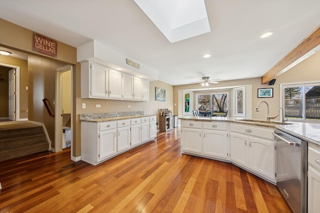 kitchen with a skylight, light wood-style flooring, stainless steel dishwasher, white cabinetry, and a sink