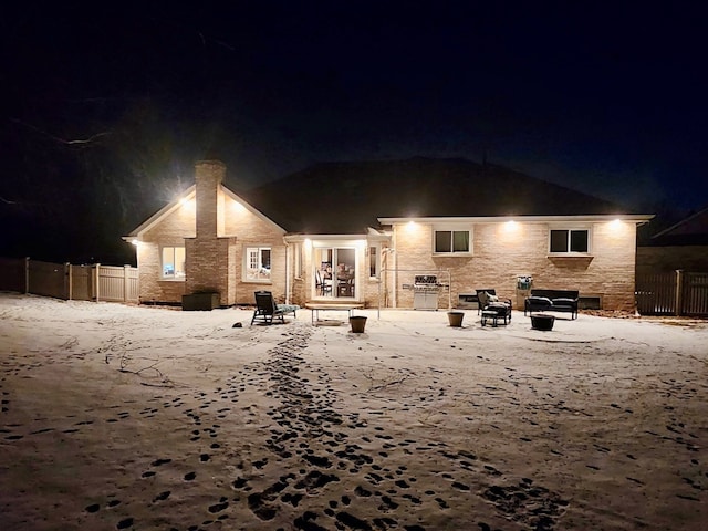 back of house at night featuring stone siding and fence