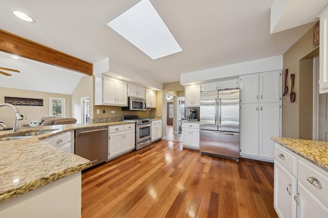 kitchen featuring vaulted ceiling with skylight, a sink, light wood-style floors, appliances with stainless steel finishes, and light stone countertops