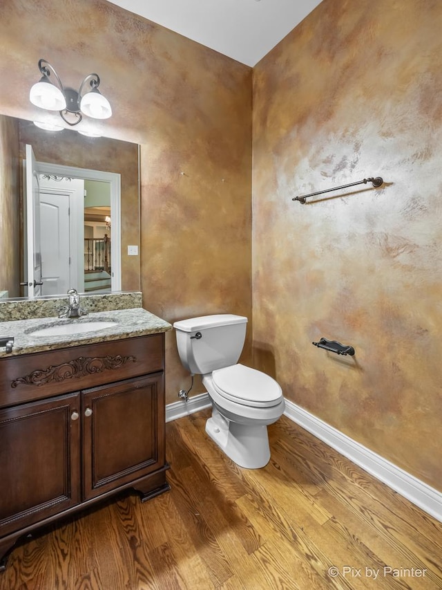 half bathroom featuring toilet, wood finished floors, vanity, and baseboards