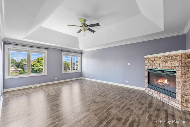 unfurnished living room featuring ceiling fan, wood finished floors, baseboards, a brick fireplace, and a tray ceiling