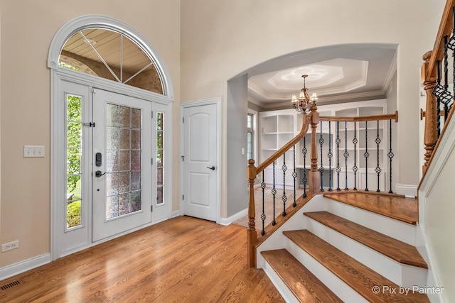 entrance foyer with arched walkways, visible vents, light wood-style flooring, an inviting chandelier, and stairs