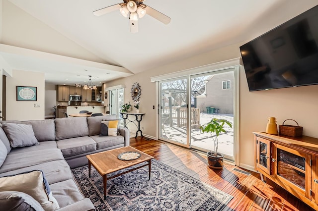 living room with lofted ceiling, ceiling fan with notable chandelier, wood finished floors, visible vents, and baseboards