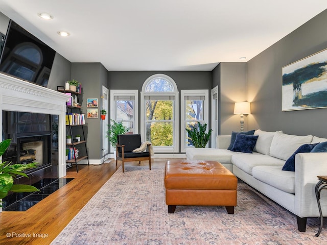 living room featuring a fireplace, baseboards, wood finished floors, and recessed lighting