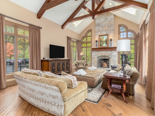 living area featuring light wood-style floors, high vaulted ceiling, beam ceiling, and a stone fireplace