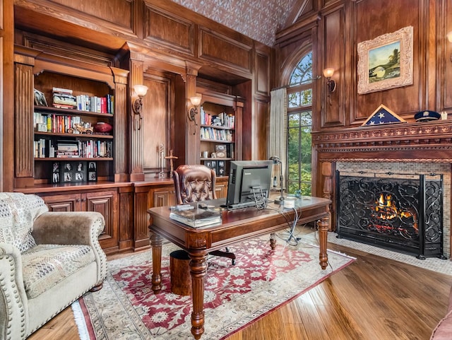 home office featuring wooden walls, a fireplace with flush hearth, light wood-type flooring, built in shelves, and high vaulted ceiling