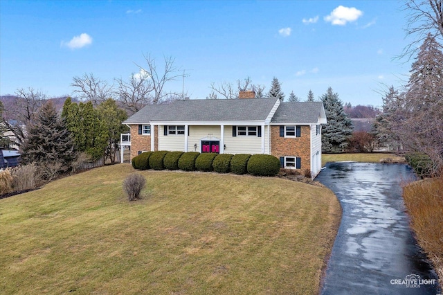 raised ranch with a chimney, a front lawn, aphalt driveway, and brick siding