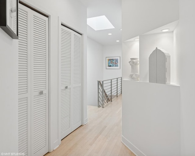 corridor featuring recessed lighting, a skylight, an upstairs landing, and light wood-style floors