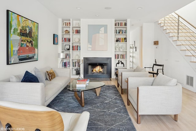 living room featuring stairway, visible vents, a lit fireplace, and wood finished floors