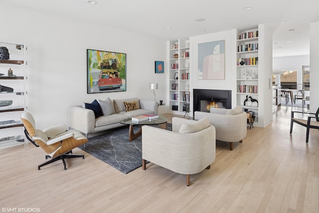 living room with built in shelves, light wood-type flooring, a glass covered fireplace, and recessed lighting