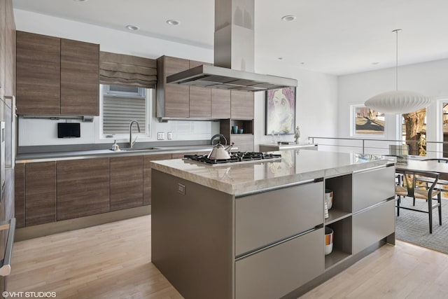 kitchen with light wood finished floors, island range hood, modern cabinets, stainless steel gas cooktop, and a sink