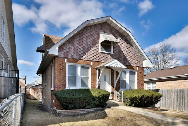 view of front facade with brick siding, a shingled roof, and fence