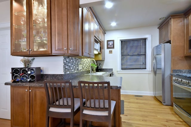 kitchen with decorative backsplash, light wood-style flooring, stainless steel appliances, a kitchen bar, and a sink