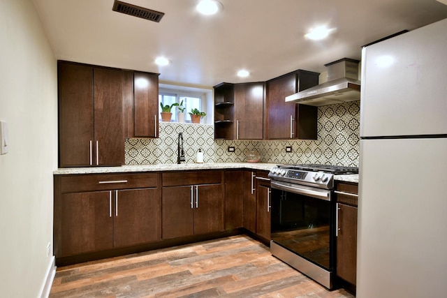 kitchen with dark brown cabinetry, visible vents, wall chimney range hood, freestanding refrigerator, and stainless steel range with gas stovetop