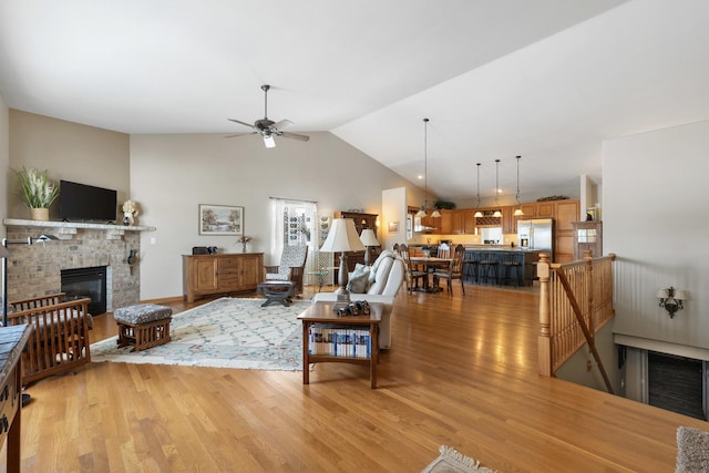 living room with light wood-style flooring, high vaulted ceiling, a ceiling fan, and a glass covered fireplace