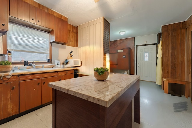 kitchen featuring light floors, light countertops, white microwave, brown cabinetry, and a sink