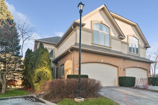 view of home's exterior with an attached garage, brick siding, driveway, roof with shingles, and stucco siding