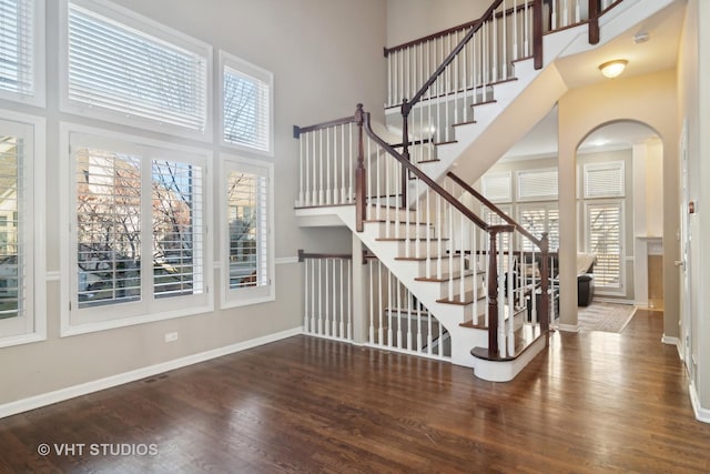 stairway featuring arched walkways, baseboards, a high ceiling, and wood finished floors