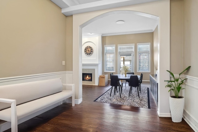 dining space with arched walkways, crown molding, wood finished floors, a warm lit fireplace, and baseboards