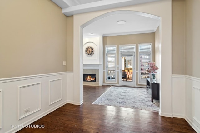 corridor featuring arched walkways, wainscoting, wood finished floors, and a decorative wall