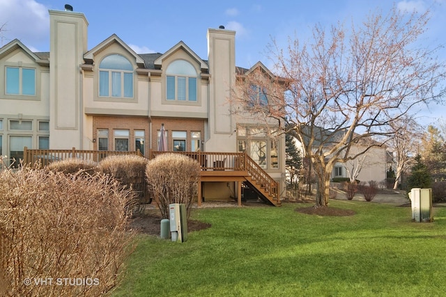 rear view of house featuring a lawn, stucco siding, stairs, a deck, and brick siding