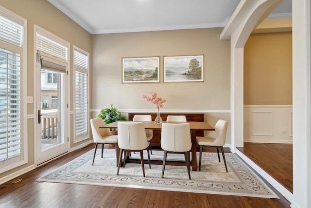 dining room featuring arched walkways, a wainscoted wall, wood finished floors, crown molding, and a decorative wall