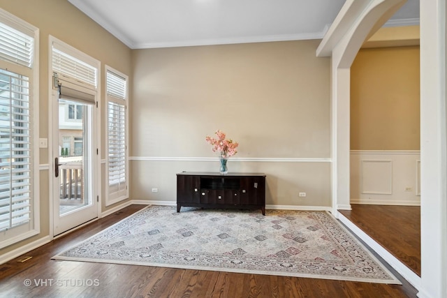 entryway featuring arched walkways, ornamental molding, wainscoting, and wood finished floors