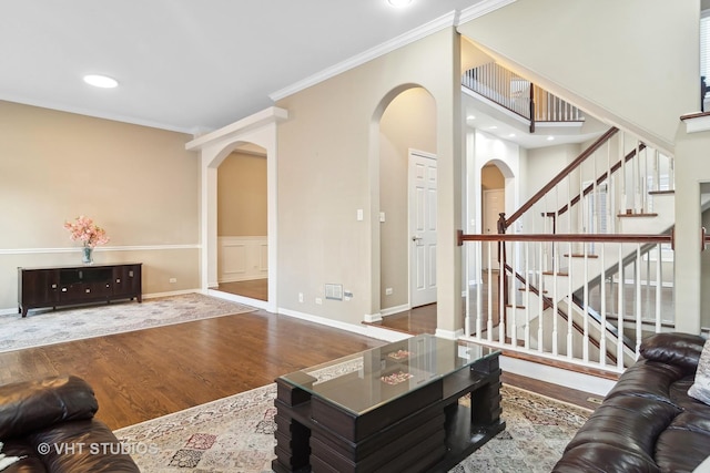 living room featuring arched walkways, stairway, ornamental molding, wood finished floors, and baseboards