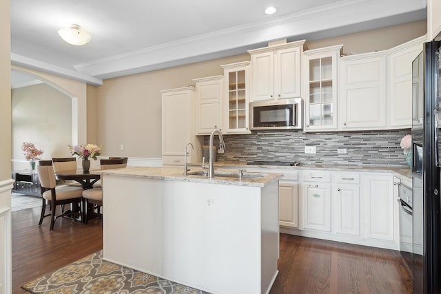 kitchen featuring arched walkways, light stone countertops, dark wood-style flooring, decorative backsplash, and stainless steel microwave