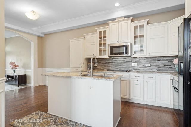 kitchen with arched walkways, dark wood finished floors, stainless steel microwave, a sink, and light stone countertops