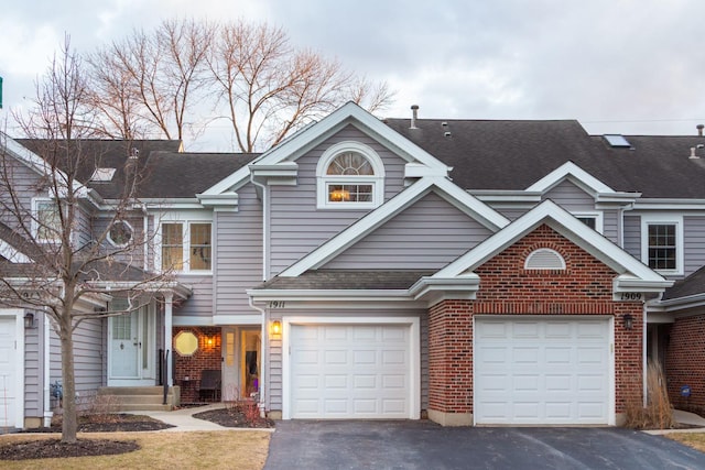 townhome / multi-family property featuring an attached garage, a shingled roof, aphalt driveway, and brick siding