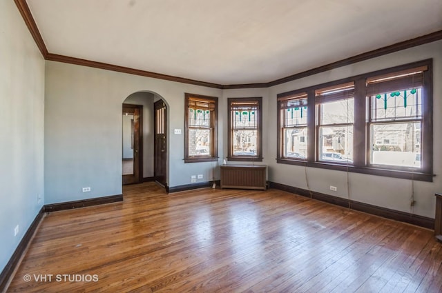 unfurnished room featuring radiator, hardwood / wood-style flooring, baseboards, and arched walkways