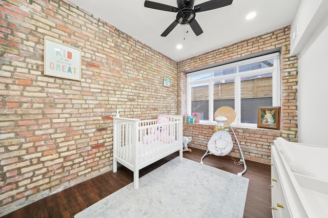 bedroom featuring ceiling fan, recessed lighting, brick wall, a crib, and dark wood finished floors