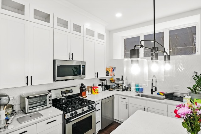 kitchen featuring glass insert cabinets, appliances with stainless steel finishes, light countertops, white cabinetry, and a sink