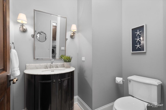 bathroom with vanity, toilet, washer / clothes dryer, and baseboards