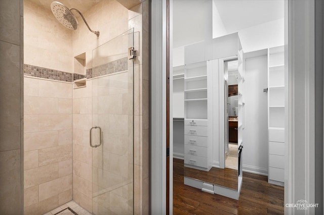 bathroom with a spacious closet, wood finished floors, and a stall shower