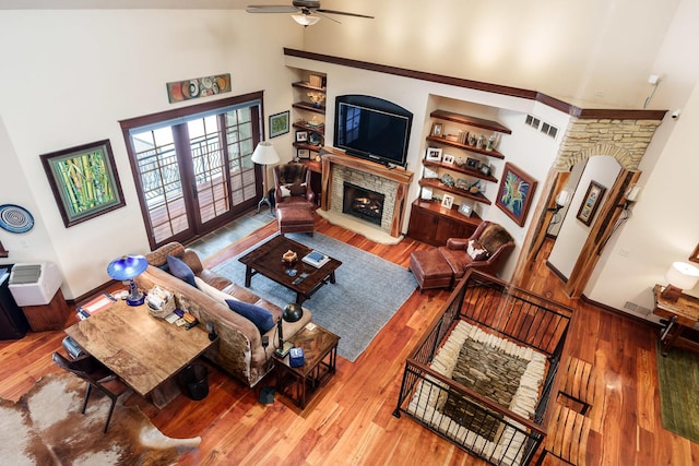 living area with visible vents, a ceiling fan, wood finished floors, a high ceiling, and a fireplace