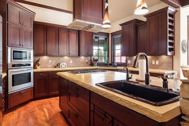 kitchen featuring stainless steel appliances, a sink, hanging light fixtures, light countertops, and island exhaust hood