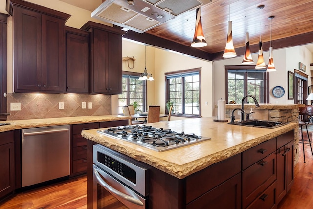 kitchen featuring a sink, hanging light fixtures, appliances with stainless steel finishes, light wood-type flooring, and backsplash