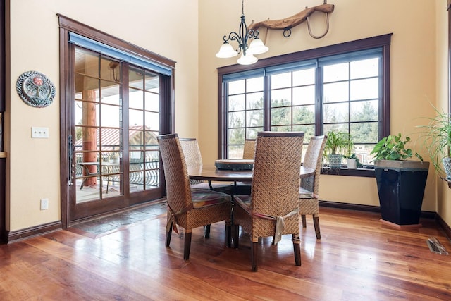 dining space featuring baseboards, wood finished floors, visible vents, and a notable chandelier