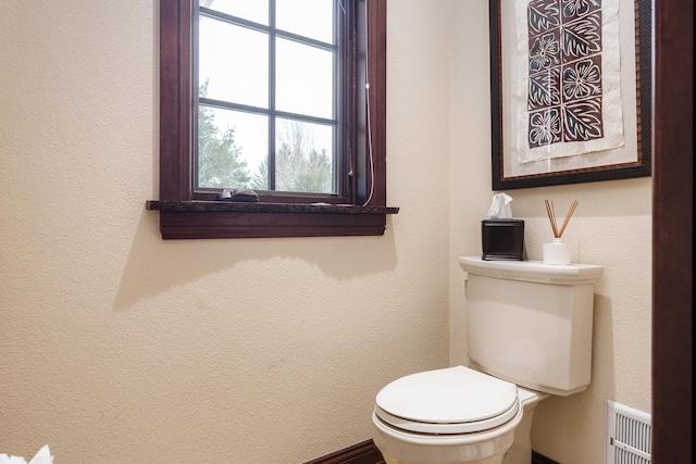 half bathroom with visible vents, a textured wall, and toilet