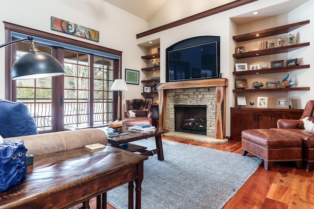 living area featuring built in features, vaulted ceiling, wood finished floors, and a stone fireplace