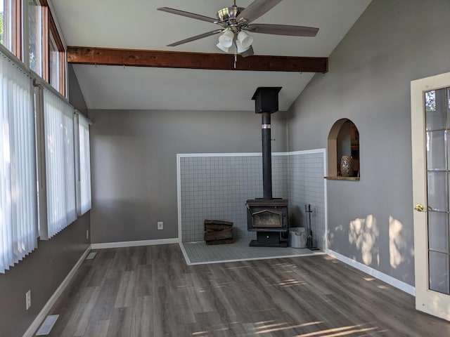 unfurnished living room with ceiling fan, baseboards, dark wood-style floors, beamed ceiling, and a wood stove