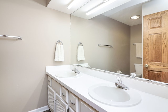 bathroom featuring double vanity, a sink, toilet, and baseboards