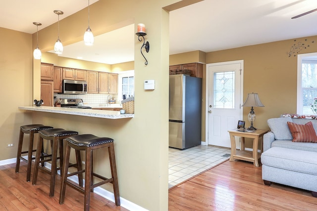 kitchen with stainless steel appliances, a breakfast bar area, backsplash, and light wood-style floors