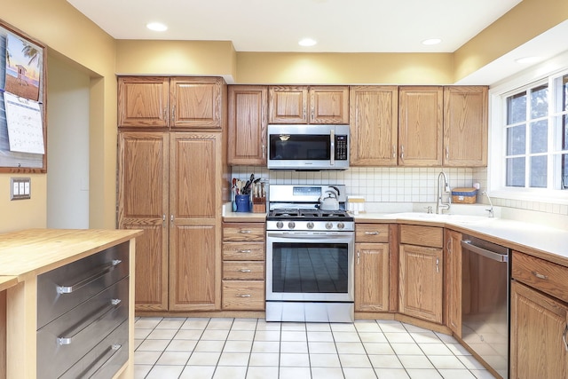 kitchen with stainless steel appliances, a sink, backsplash, and light tile patterned floors